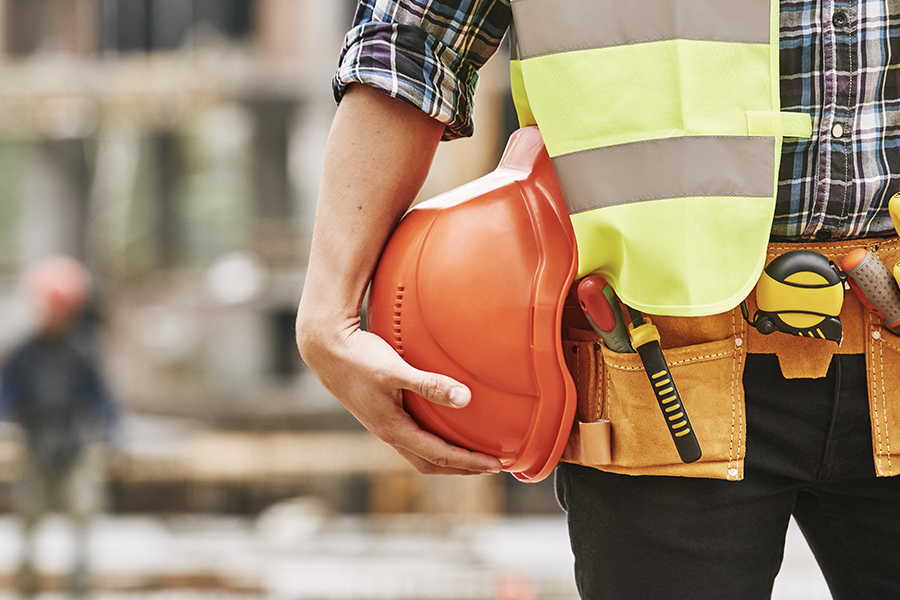 Specialized Business Insurance - Cropped Photo of Construction Worker with Tools Holding a Safety Helmet while Standing Outdoors in Front of a Construction Site